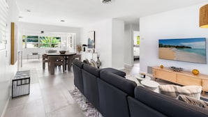 A modern living room with a dark sofa, a wooden sideboard, and a large beach-themed painting. - Oasis Backyard With Heated Pool Oakland Park (Wilton Manors)