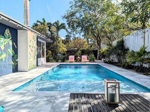 Une piscine avec une terrasse en bois, deux chaises longues et une petite table.