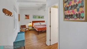 A bedroom with a bed, a bench, a chair, a nightstand, and a window. - Castaways Casita Saltwater Pool Dog Friendly (Fort Lauderdale)
