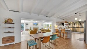 A spacious living area with a wooden dining table, orange and teal chairs, and a view of the kitchen and dining room through an open archway. - Castaways Casita Saltwater Pool Dog Friendly (Fort Lauderdale)