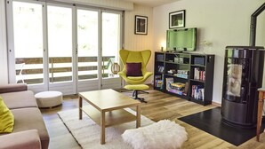Uma sala de estar com sofá, poltrona amarela, mesa de centro, estante, lareira e porta de vidro deslizante para área externa.