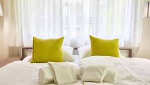 Quarto de hotel com cama, duas almofadas e janela com cortinas leves.