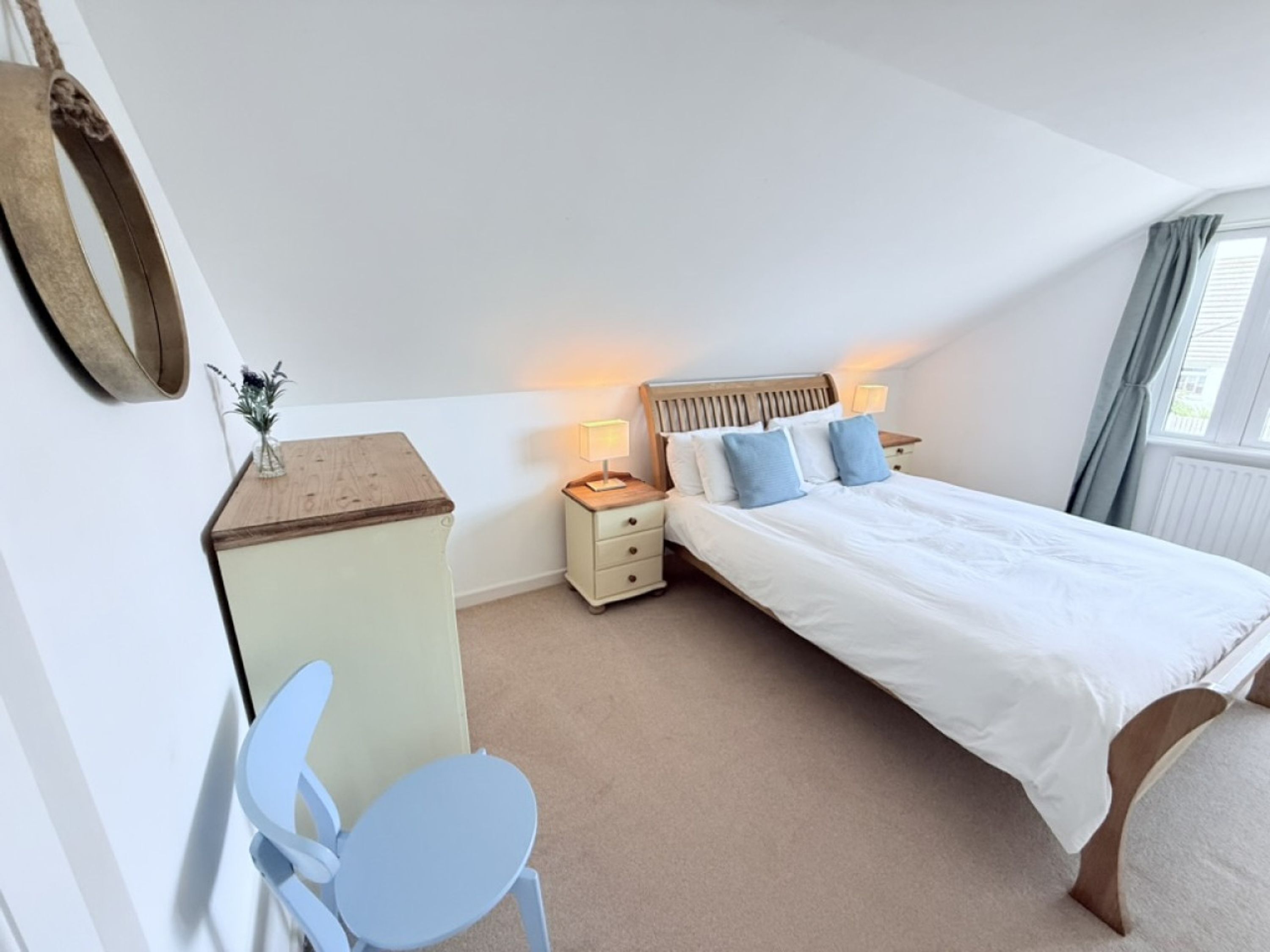 Een slaapkamer met een bed, nachtkastje, lamp, stoel en een bureau met spiegel.