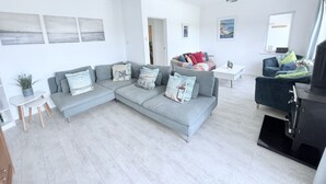 A modern living room with a grey sectional sofa, a black cabinet, and a small side table. - Meadow View in Widemouth Bay (Bude)