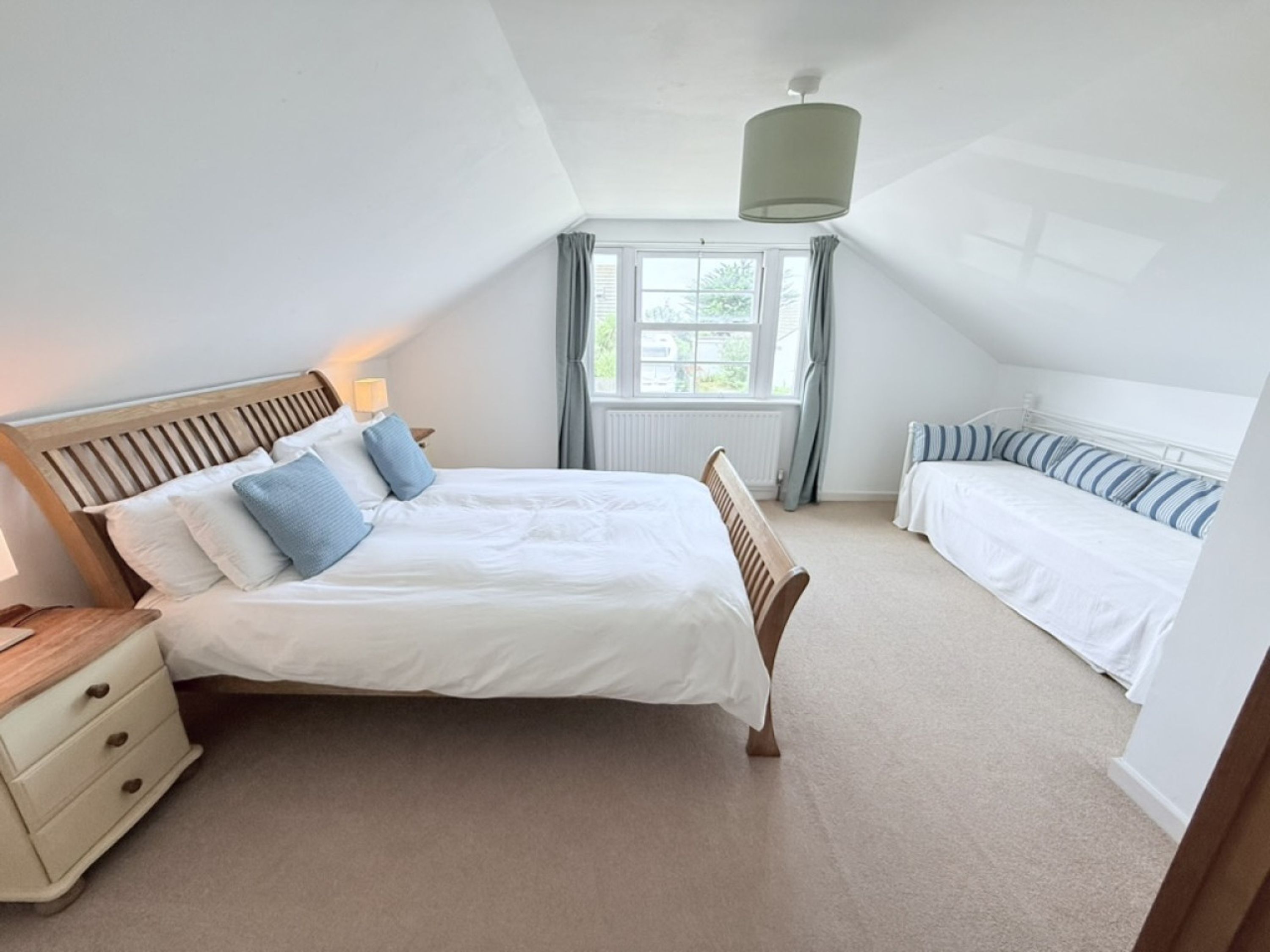A bedroom with a large bed, a smaller bed, a nightstand, and a window with curtains.