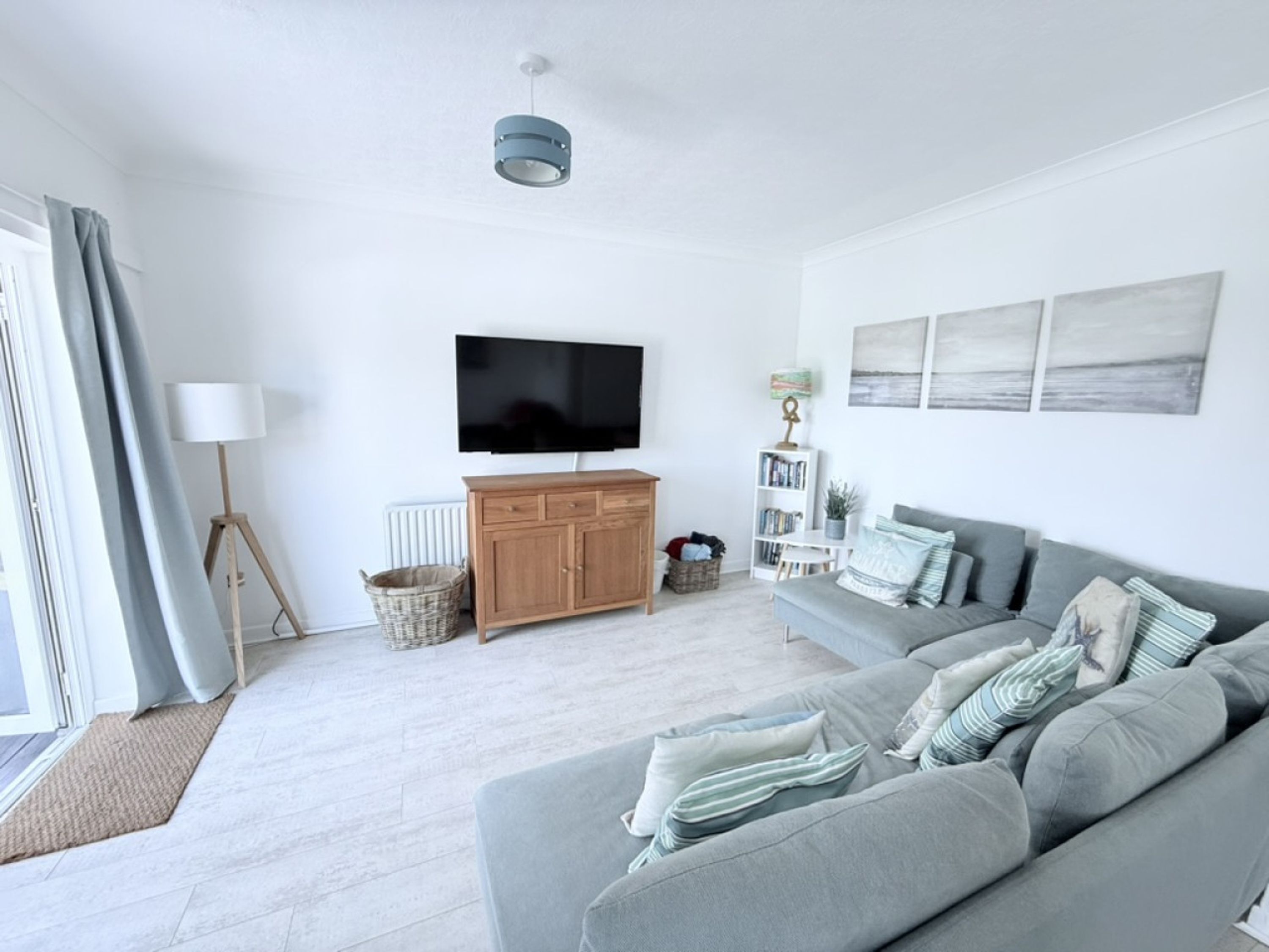 A modern living room with a grey sofa, a flat-screen TV, a wooden cabinet, and a bookshelf.