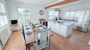 A spacious kitchen with wooden flooring, white cabinetry, a central island, and a built-in oven. - Meadow View in Widemouth Bay (Bude)
