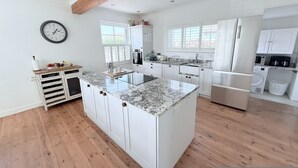 A modern kitchen with white cabinetry, a granite countertop island, and wooden flooring. - Meadow View in Widemouth Bay (Bude)