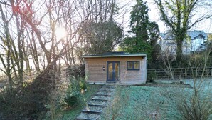 A small wooden cabin with a dark door, surrounded by a grassy area and trees. - The Cabin in Lifton With 1 Bedrooms and 1 Bathrooms (Lifton)