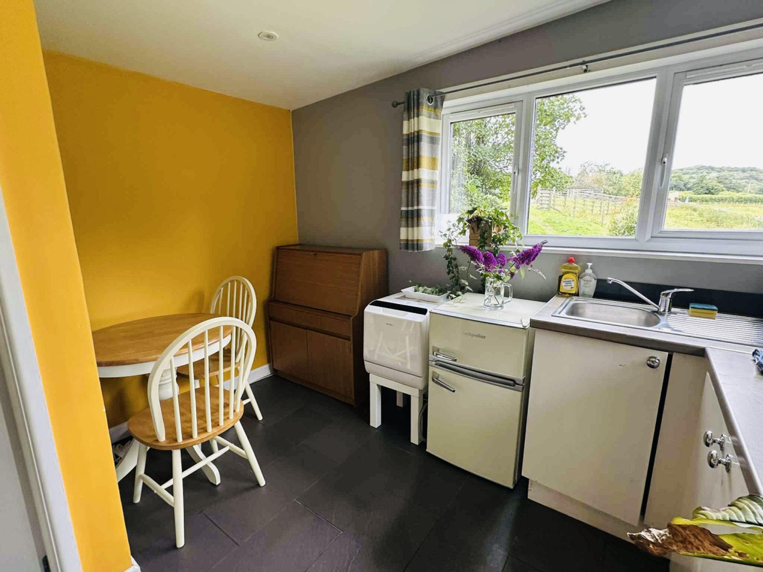 Una cocina compacta con una mesa y sillas, un refrigerador, un lavamanos y un ventanal con vistas al verdor.