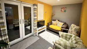 A living room with a sofa, a television, and a sliding glass door leading to a balcony. - The Cabin in Lifton With 1 Bedrooms and 1 Bathrooms (Lifton)