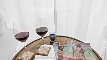 A round wooden table with two wine glasses and a small glass of water, surrounded by magazines on a white curtain backdrop.