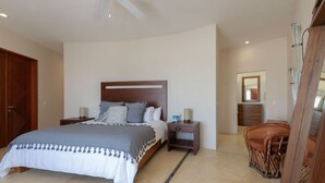 A bedroom with a large bed, bedside tables, a nightstand, a wooden chair, and a mirror on the wall. - Casa Caracol - Mita Residential Farallon (Punta de Mita)
