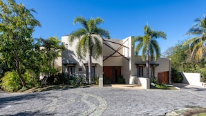 A modern building with a stone-paved entrance, surrounded by palm trees and greenery. - Casa Caracol - Mita Residential Farallon (Punta de Mita)