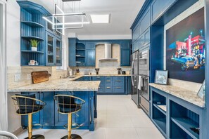A modern kitchen with blue cabinetry, a granite countertop, and two bar stools.