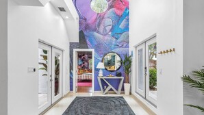 A modern hallway with a large digital art installation on the wall, a grey rug, and a console table with a mirror and decorative items. - Chic Retreat Heated Pool Floats Close to Beach (Fort Lauderdale)
