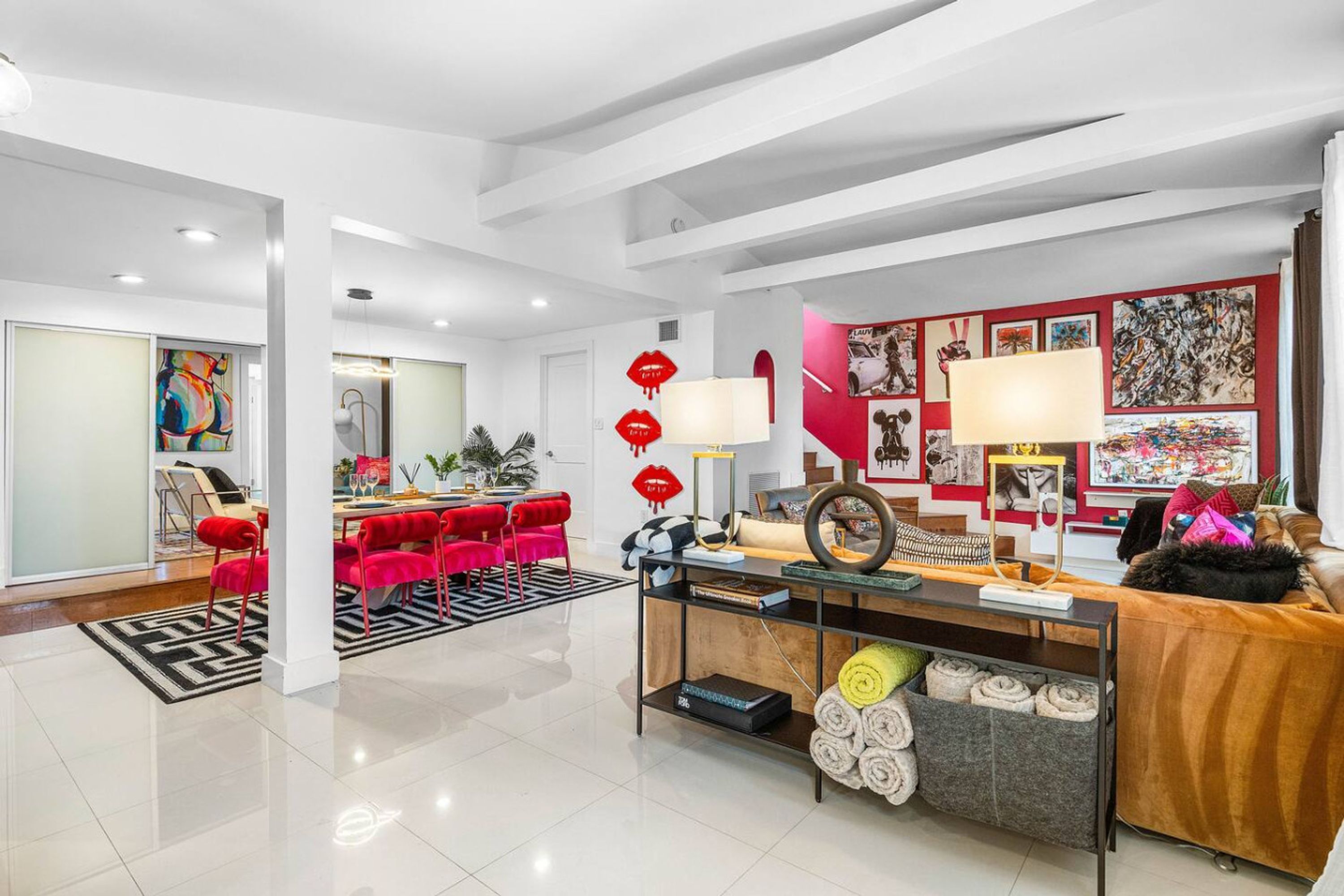 A modern living room with a dining area, featuring a red sofa, a coffee table, and a wall adorned with artwork.