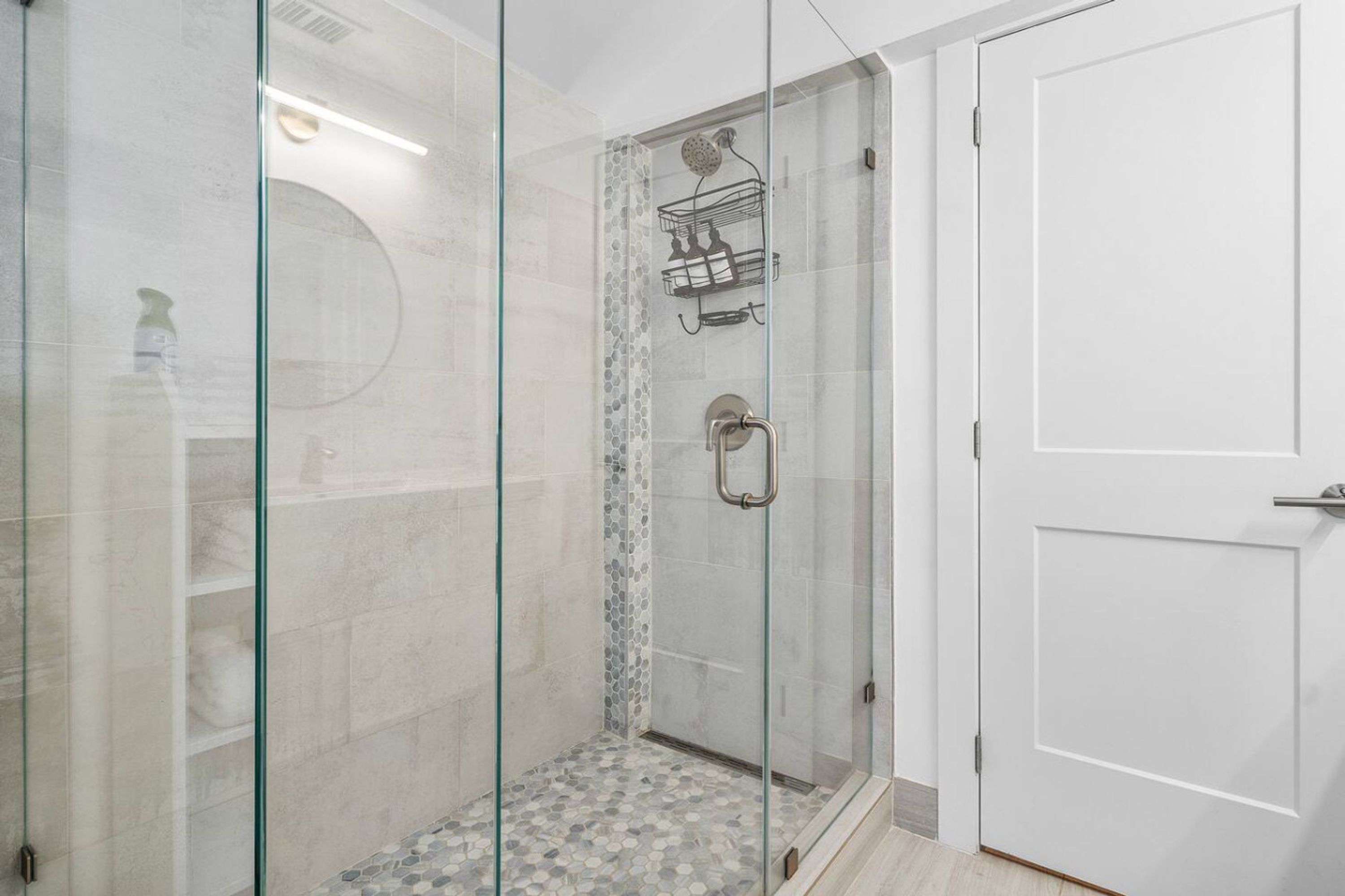 A glass-enclosed shower with a tiled floor and a shower caddy.