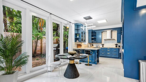A modern kitchen with blue cabinets, a central island, and a dining area with a round table. - Chic Retreat Heated Pool Floats Close to Beach (Fort Lauderdale)