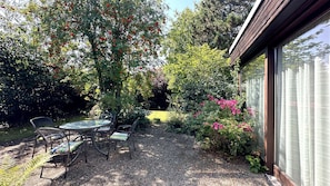 A patio with a table and chairs, surrounded by lush greenery and flowering plants. - 128 sqm/4 rooms: sunny feel-good bungalow with garden (Braunschweig)