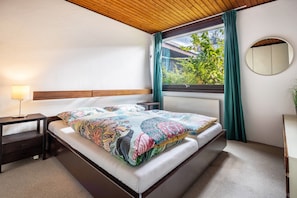 A bedroom with a bed, bedside table, lamp, window with curtains, and a round mirror on the wall. - 128 sqm/4 rooms: sunny feel-good bungalow with garden (Braunschweig)