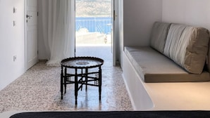 A modern, minimalist room with a large window, a round table, a sofa, and a ceiling light fixture. - Aerase Apartment in Karpathos (Karpathos)
