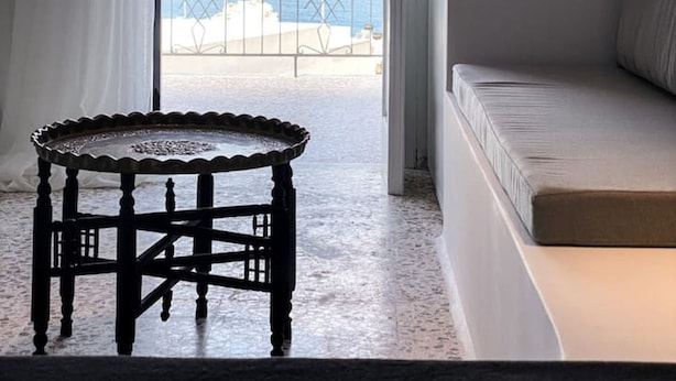 A room with a view of the sea, a balcony with a metal railing, a round wooden table, and a sofa. - Aerase Apartment in Karpathos (Karpathos)