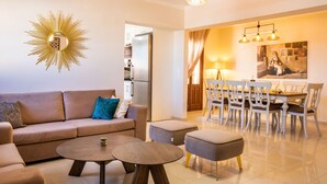 A modern living room with a sofa, ottoman, coffee table, and a dining area with a chandelier. - Villa Danai in Volada (Karpathos)