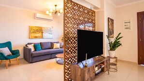 A modern living room with a flat-screen TV, a sofa, a decorative partition, and a potted plant. - Villa Danai in Volada (Karpathos)