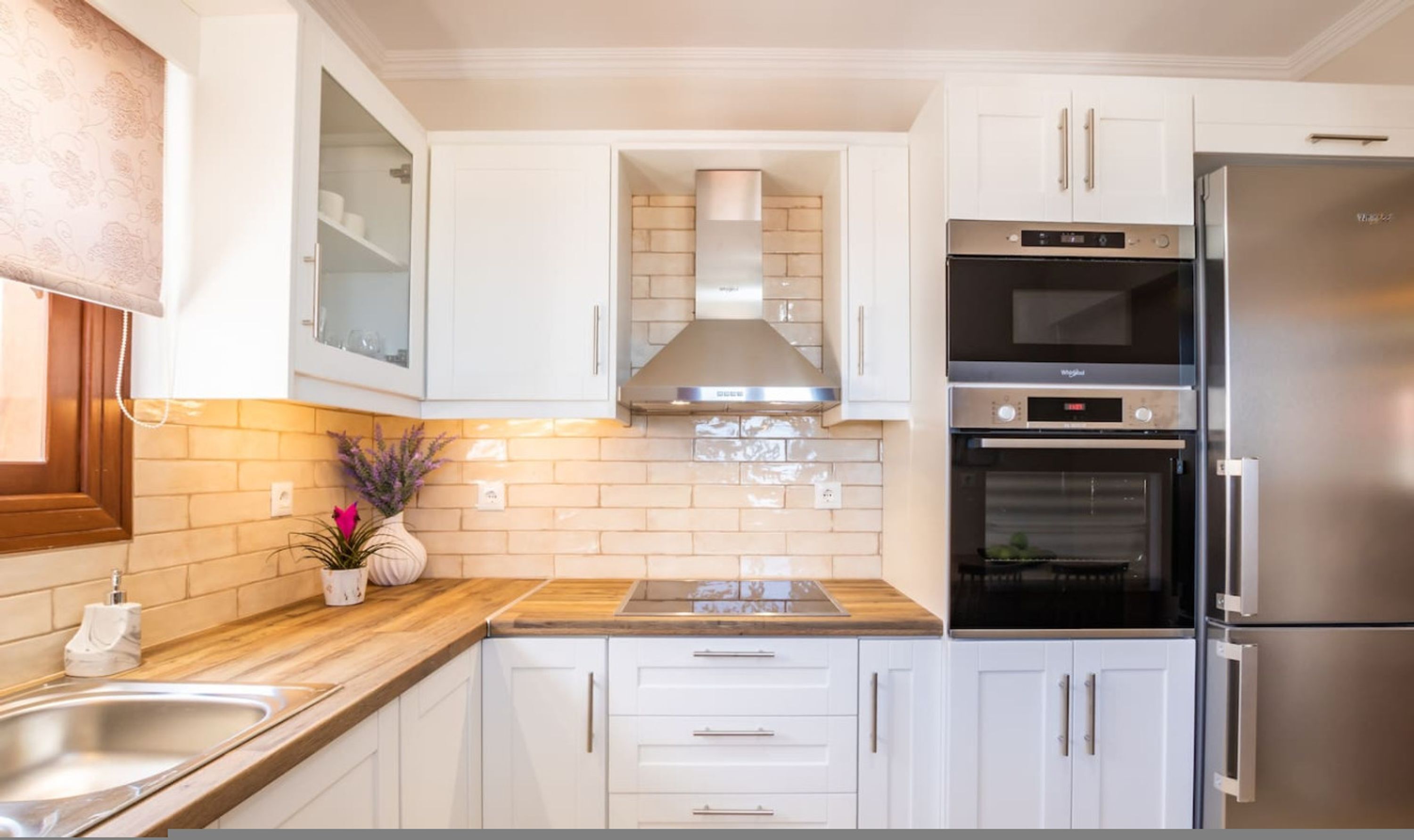 Una cocina moderna con armarios blancos, un refrigerador de acero inoxidable, horno empotrado y encimera de madera.