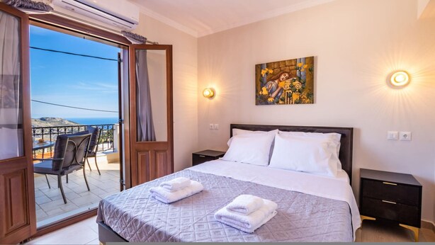 A hotel room with a bed, a painting, and a balcony with a view. - Villa Danai in Volada (Karpathos)