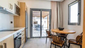 Une cuisine moderne dotée d’appareils électroménagers intégrés, un coin repas avec une table ronde et des chaises en cuir, et une porte-fenêtre coulissante donnant sur un patio extérieur.