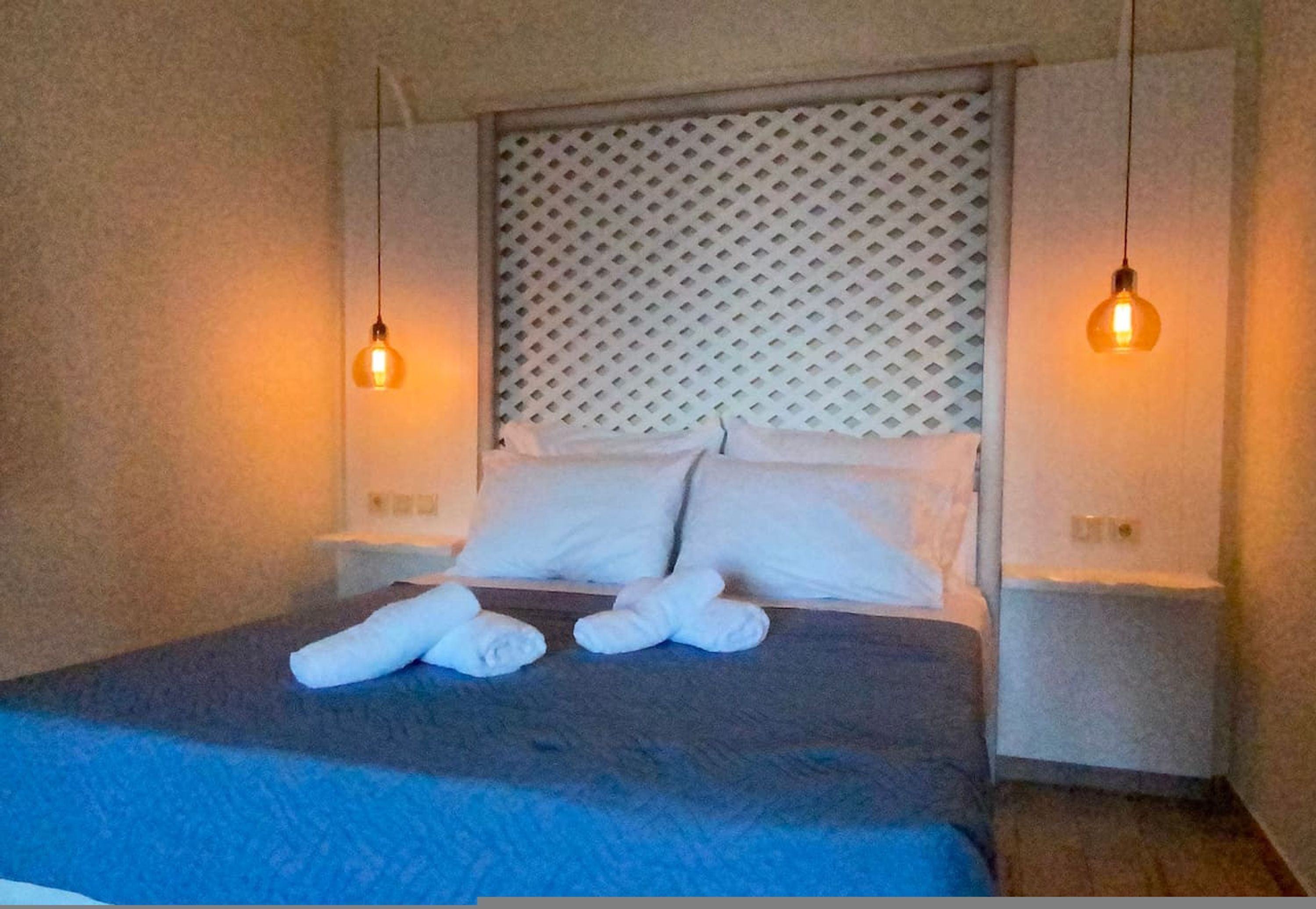 A neatly made bed with white pillows and a blue blanket, two bedside lamps, and a textured headboard.