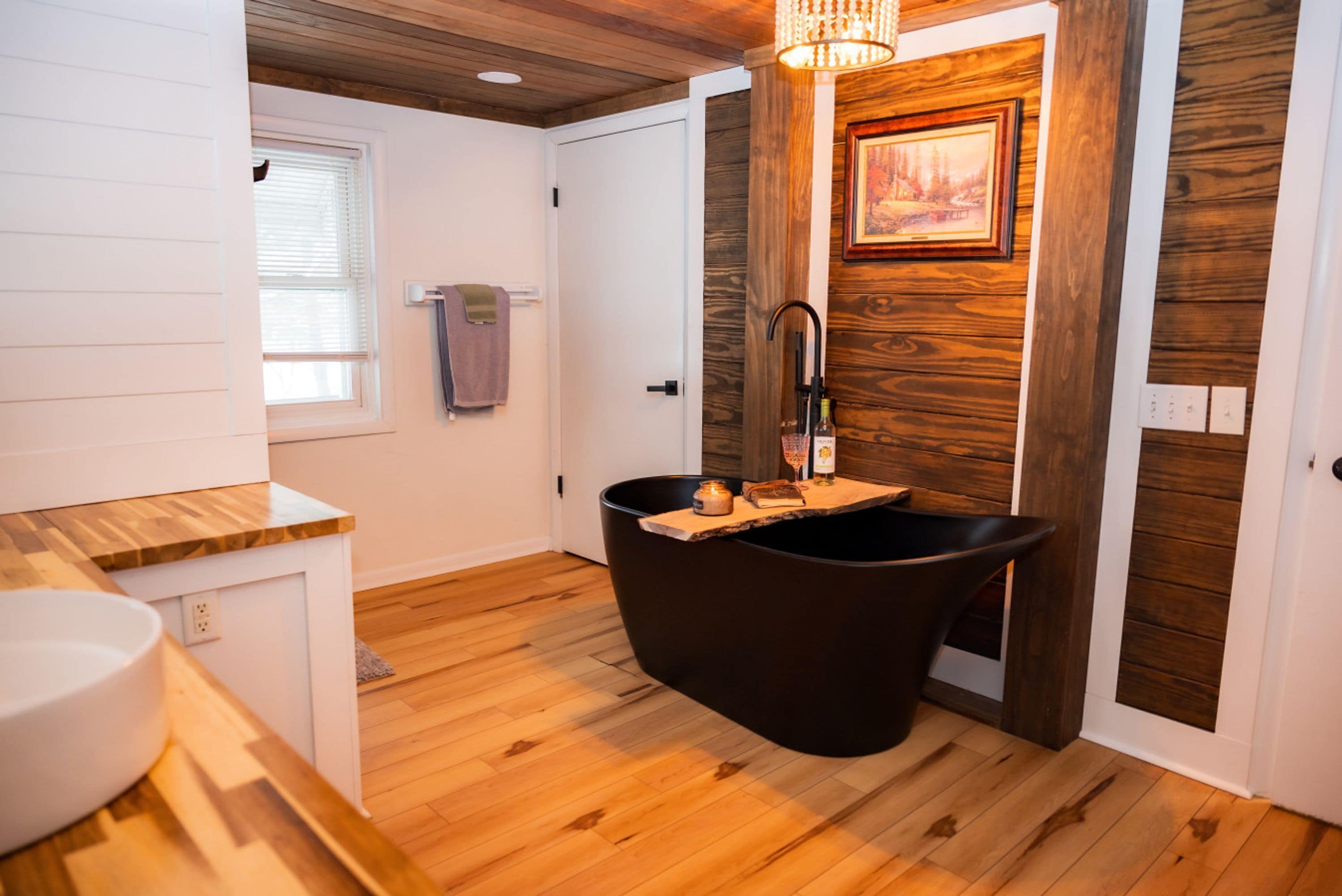 Une salle de bain moderne avec une baignoire sur pieds, un lambris mural en bois et un lavabo blanc.