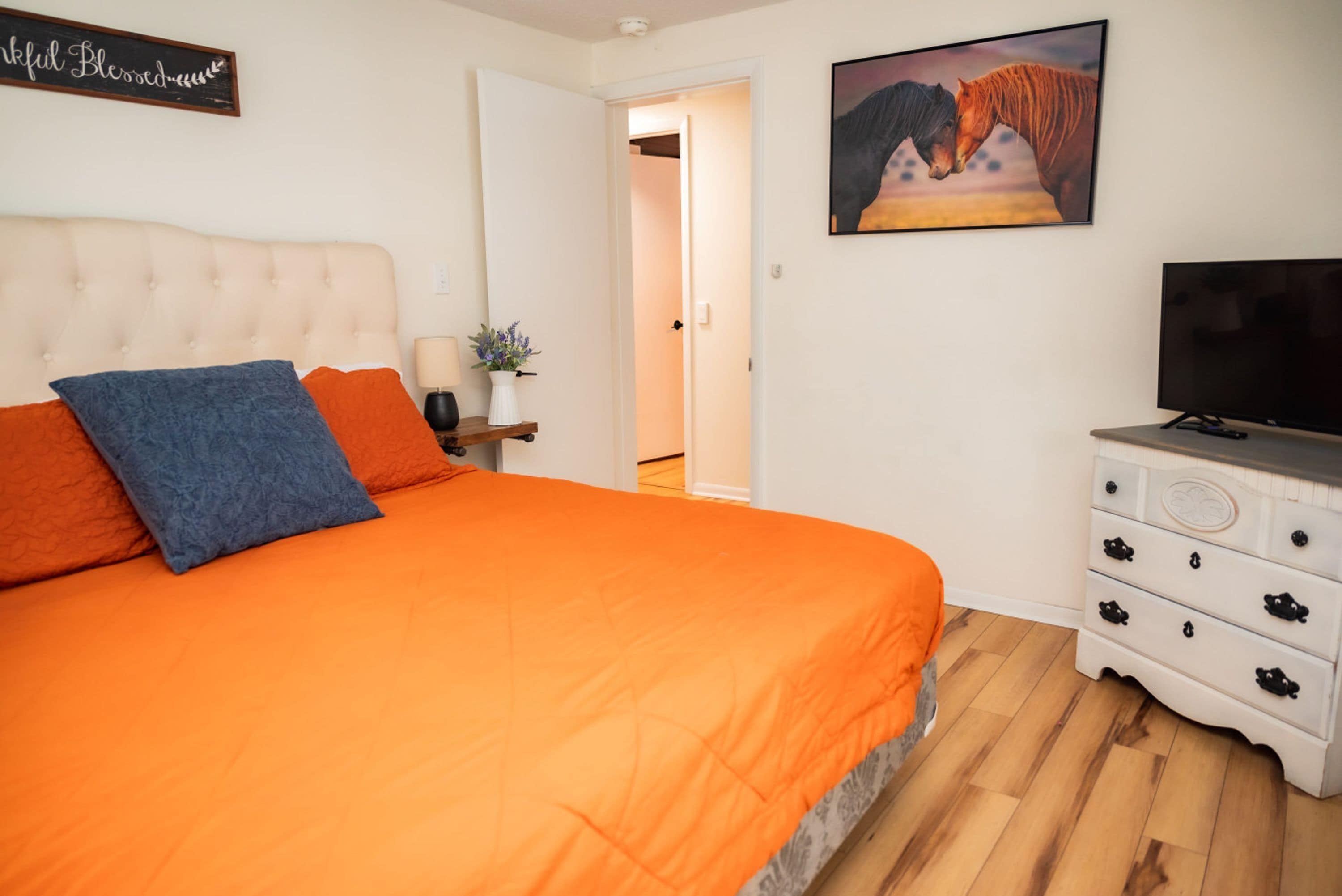 A bedroom with a large bed, a television, a dresser, and a painting on the wall.