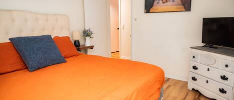 A bedroom with a large bed, a television, a dresser, and a painting on the wall.