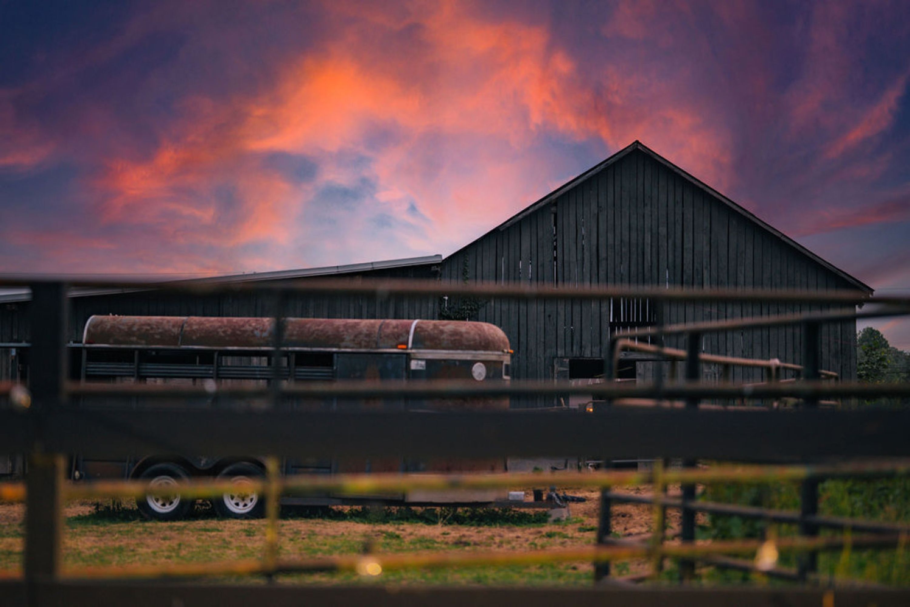 A barn with a trailer in front, under a colorful sky.