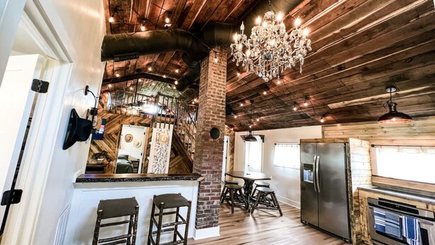 A rustic kitchen with wooden beams, a chandelier, and a brick wall.
