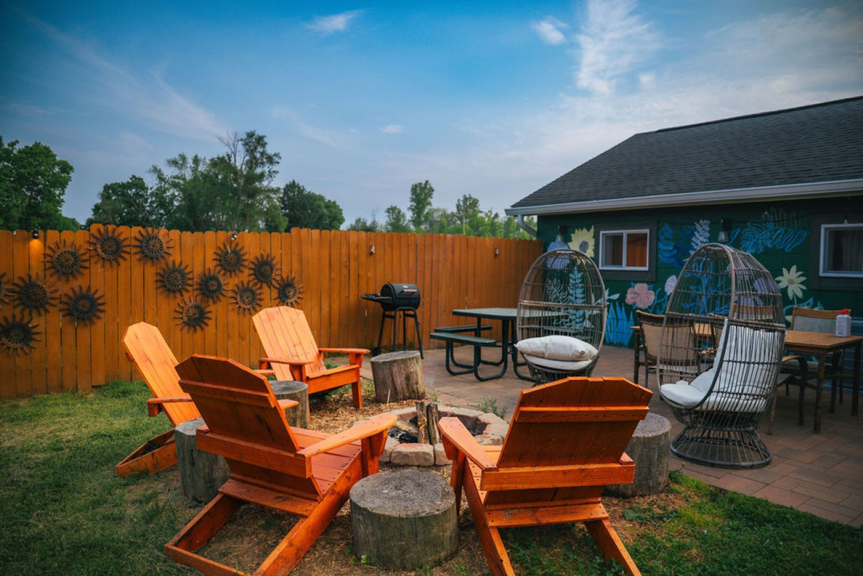 A backyard with wooden chairs, a table, and a fire pit.