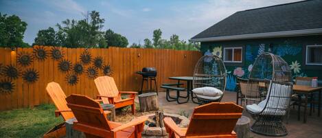 A backyard with wooden chairs, a table, and a fire pit.