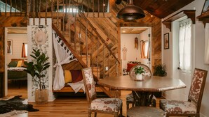 A rustic interior with a wooden staircase, a round dining table, and chairs with animal print upholstery.