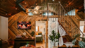 A rustic room with a wooden ceiling, a bed with a green blanket, a television, and a staircase.