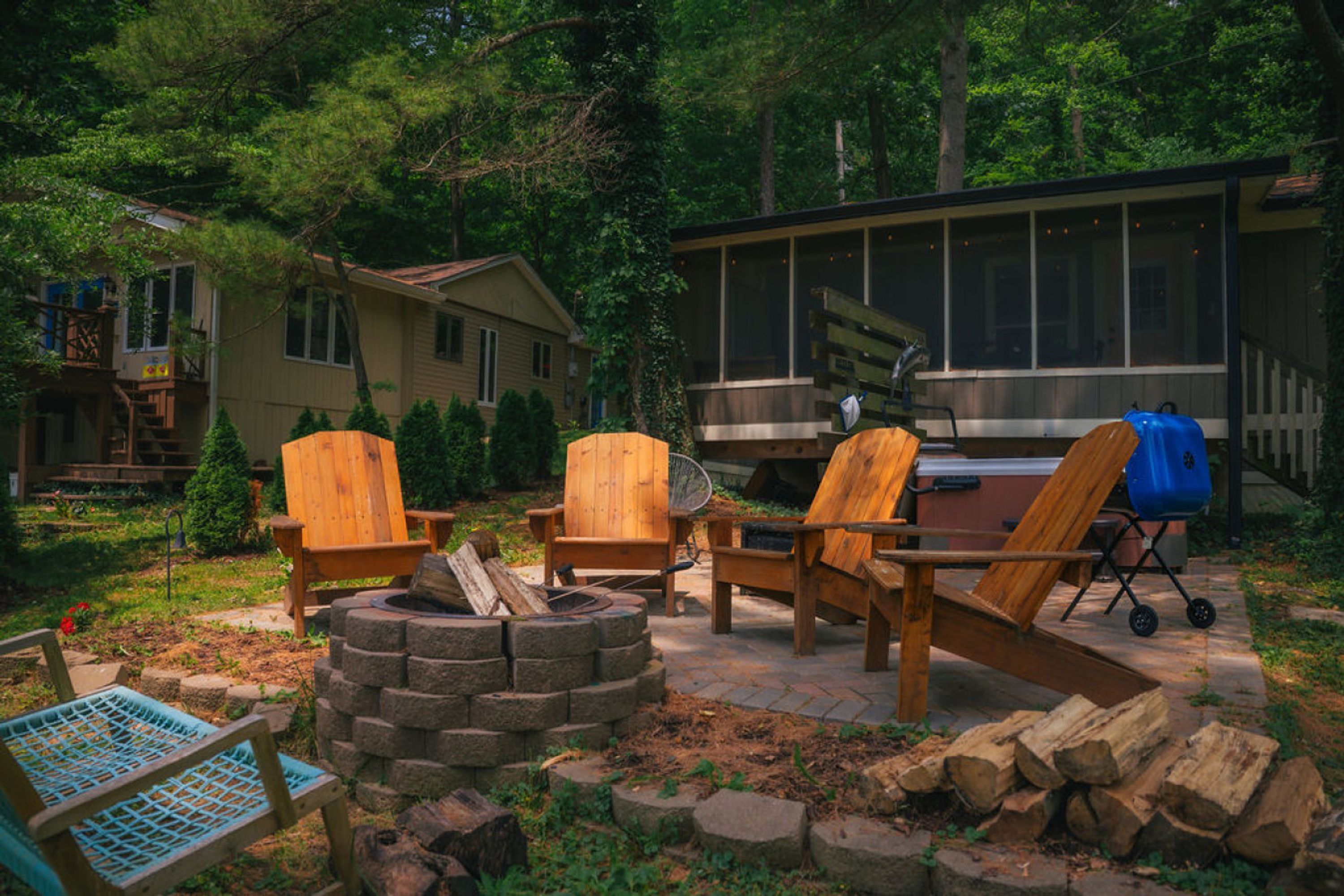 A backyard with a fire pit, wooden chairs, a grill, and a deck.