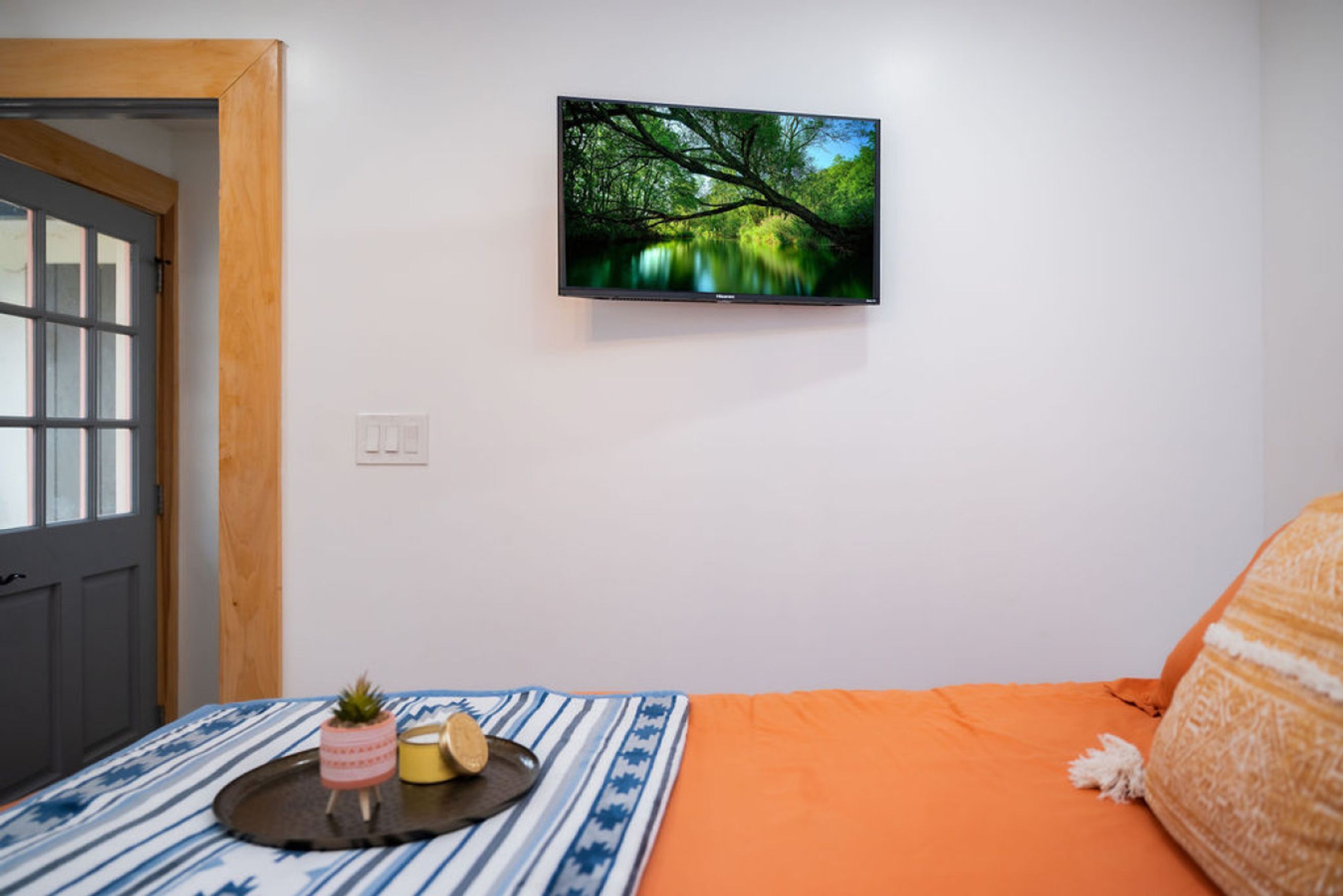 A bedroom with a bed, a television mounted on the wall, and a small table with a plant and a cup.