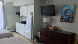Hotellihuone, jossa on kaksi sänkyä, pieni keittiönurkkaus, televisio, taulu ja kattotuuletin.