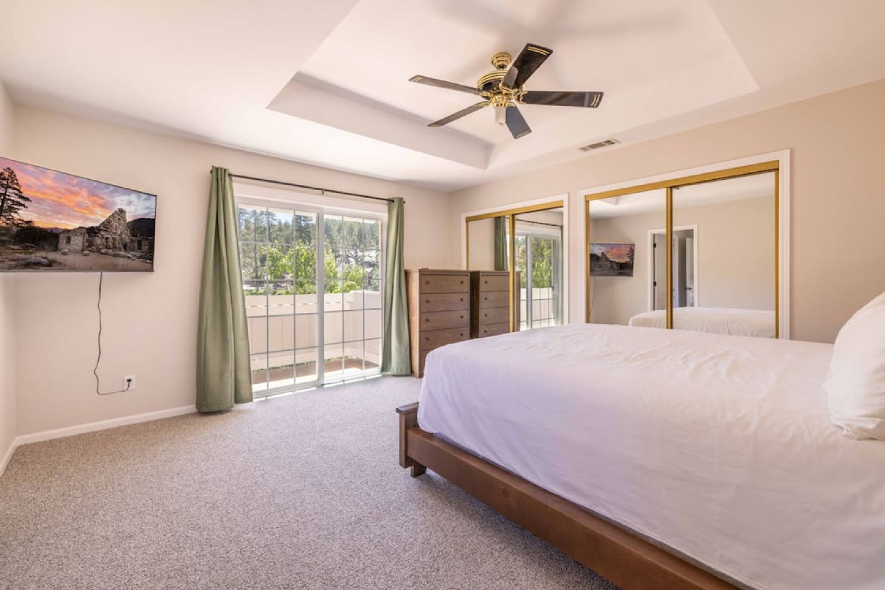 Una camera da letto con un letto grande, un ventilatore a soffitto, una porta scorrevole in vetro che dà su un balcone e un quadro appeso al muro.