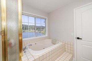 Een badkamer met een badkuip, een raam met uitzicht op een meer, en een witte deur.