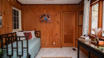 A cozy room with wooden walls, a bed with a blue bedspread, a wooden door, and a window with curtains.