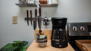 Une cuisine équipée d’une machine à café, de couteaux et d’une étagère avec des bocaux et une plante.