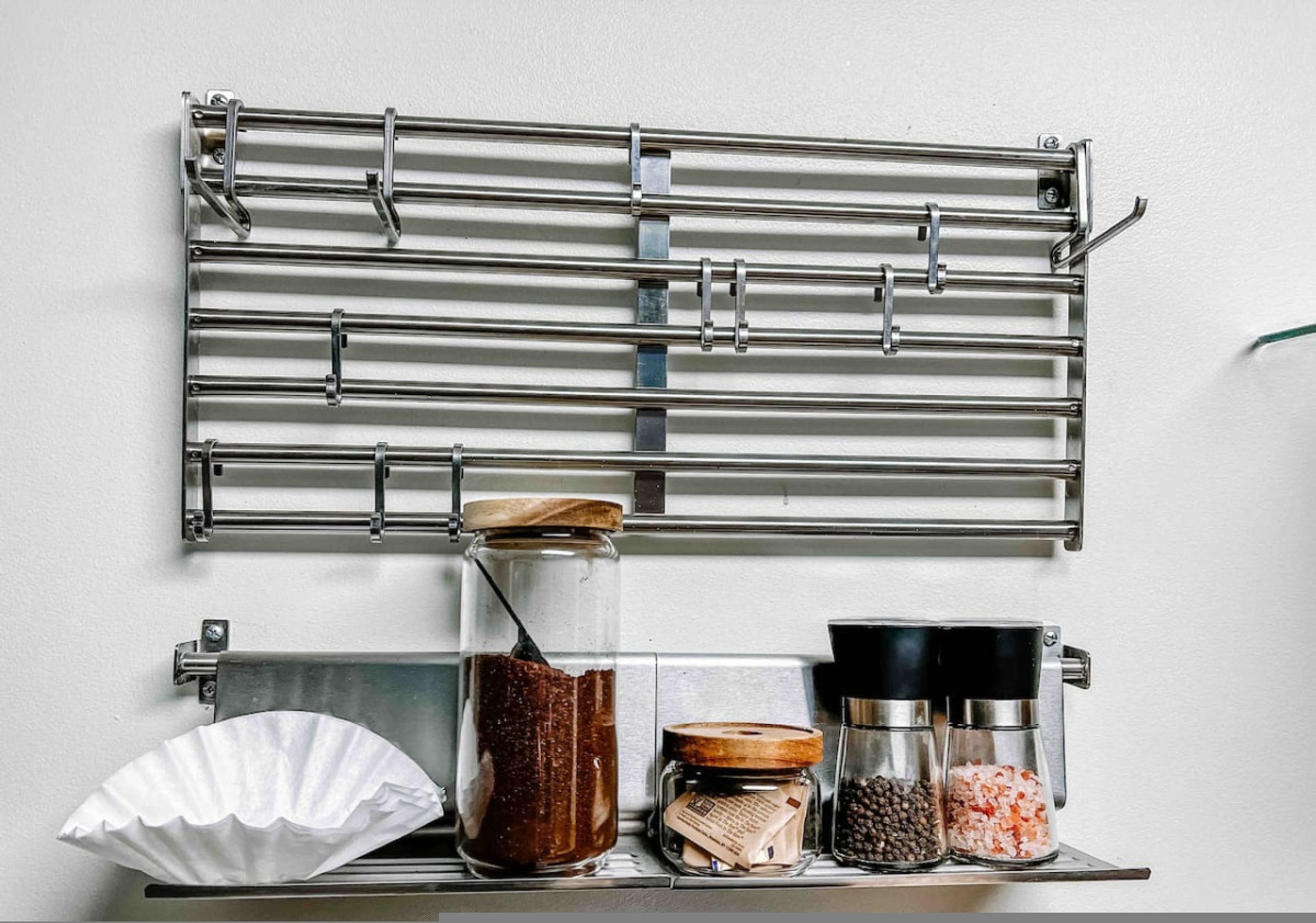 Une cuisine équipée d’une étagère métallique où sont rangés des bocaux et des récipients, d’une machine à café et d’un porte-essuie-tout.